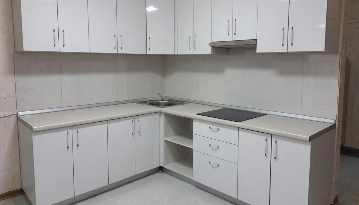 Типовая готовая кухня из магазина с прямым гарнитуром и белыми глянцевыми фасадами. Видны щели между шкафами и стеной, закрытые плинтусами.