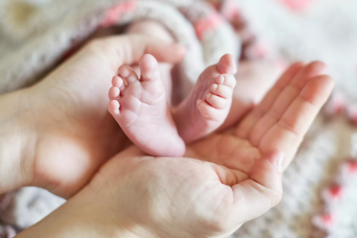 Женщина держит ножки новорожденного в своих руках | © iStock.com / encrier
