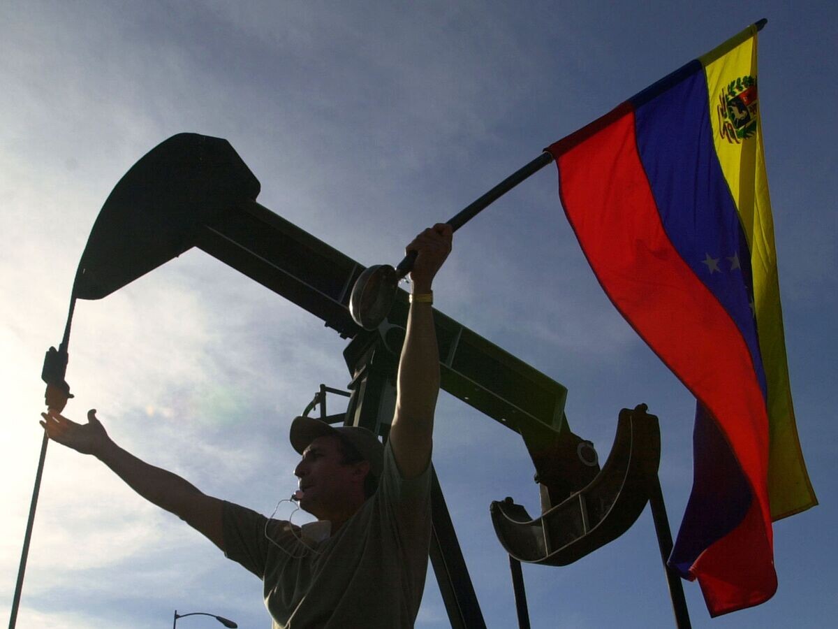    Мужчина с флагом Венесуэлы перед зданием компании PDVSA в Каракасе | © AP Photo / Fernando Llano