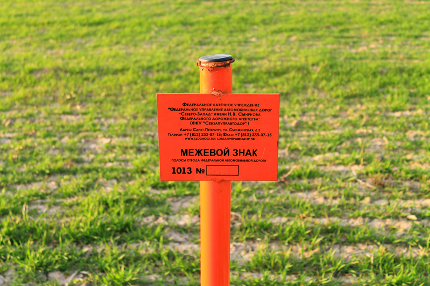 Межевой знак полосы отвода федеральной автомобильной дороги на фоне зеленого поля