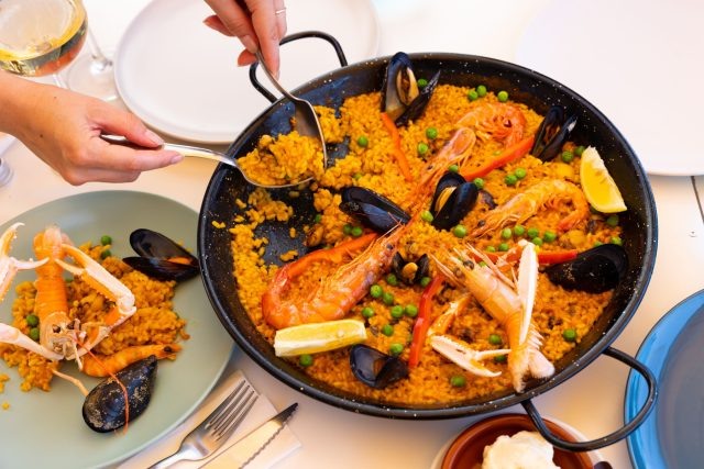 Паэлья подаётся прямо в широкой сковороде, в которой готовилась: рис с шафраном впитывает бульон и морепродукты, а на дне образуется сокоррат — тонкая поджаристая корочка. Её едят сразу, потому что текстура и корочка важны именно в моменте.  📷
