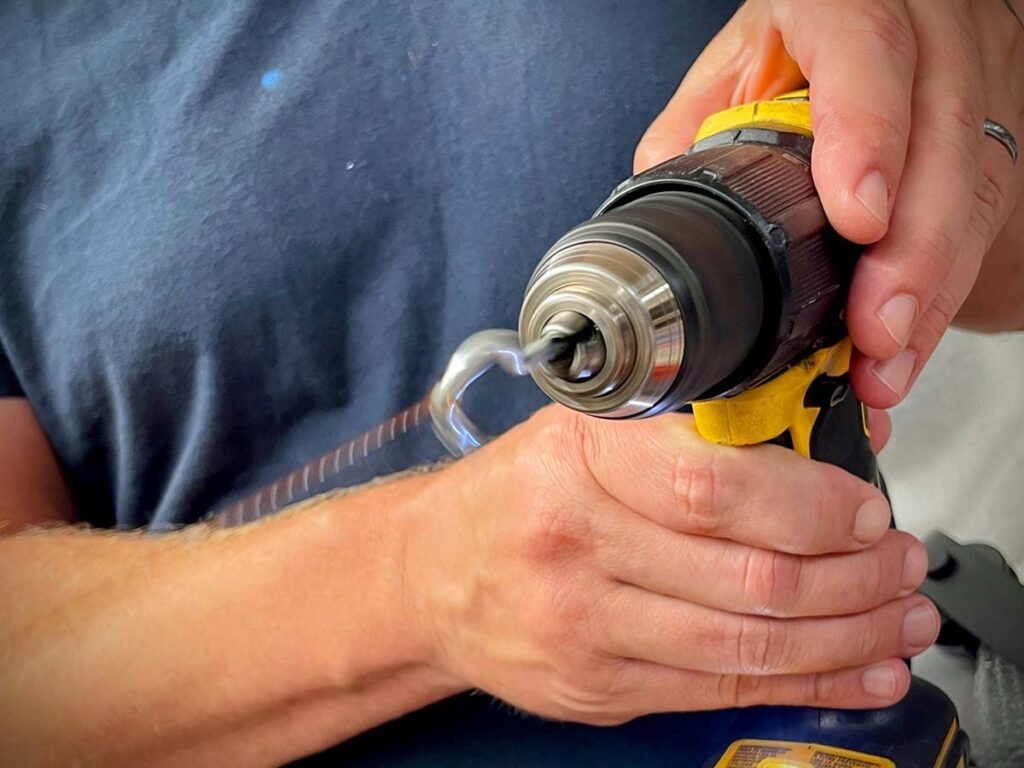 Возьмите крючок, закрепленный в ручной дрелью, и зацепите им большую петлю. Натяните петлю и включите дрель. Держите натяжение постоянным, потому что проволока будет притягиваться к тискам по мере скручивания.