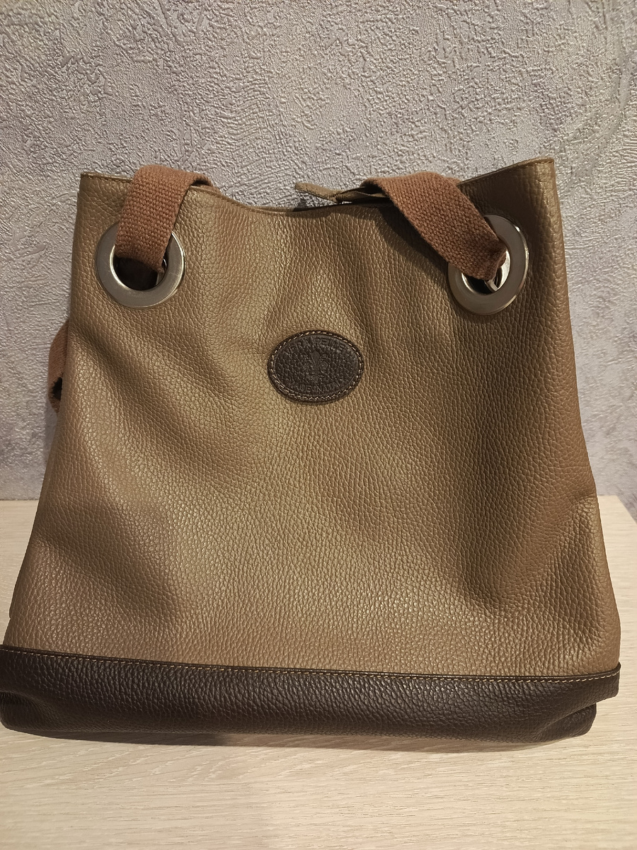 У сумки две ручки из тканевого ремня, оплетенного кожей.