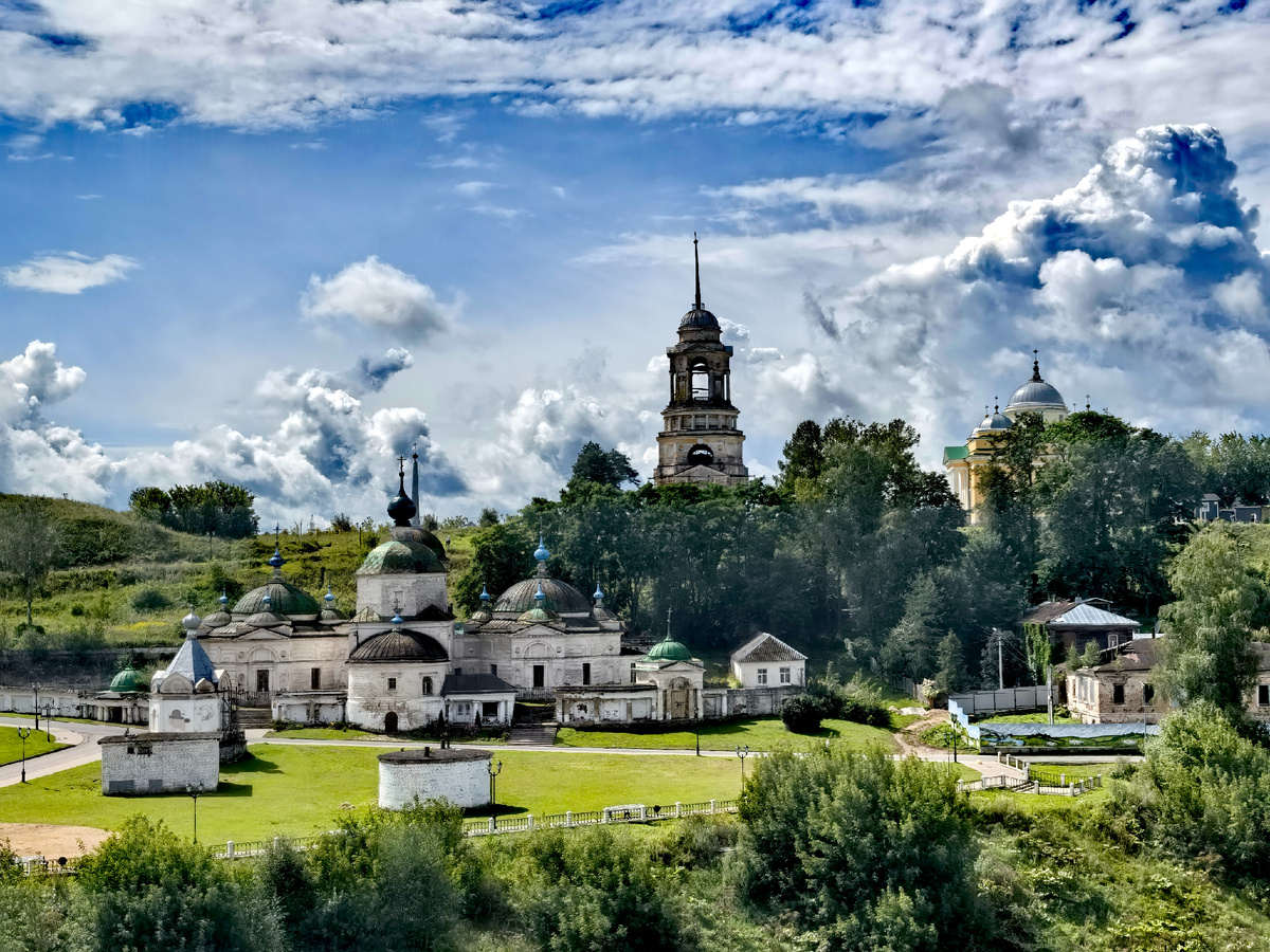 Бывают виды, которые заставляют сердце биться чуть медленнее. Эта панорама — как ожившая картина классика: белокаменные храмы с изумрудными куполами, гордая колокольня, возвышающаяся над кронами деревьев, и небо, которое превратило облака в настоящие горы.