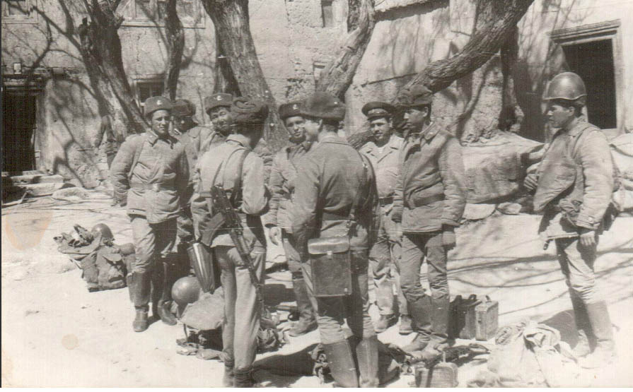 На правом фланге стоит Салман Цечоев зкв. 4-го взвода, рядом боец со смуглым азиатским лицом – Рома Дасаев. Между головами Ромы и Салмана виден Витя Щербина. Спиной к нам два офицера: Ротный с автоматом на плече и Старцев с полевой сумкой. Между Ротным и Старцевым лицом к нам Серёга Кондрашин, рядом с ним, в фуражке, Старшина прапорщик Зюзин, далее худощавый солдат Байрамалиев (Бармалей). В бронике и каске - рядовой Борисов. 