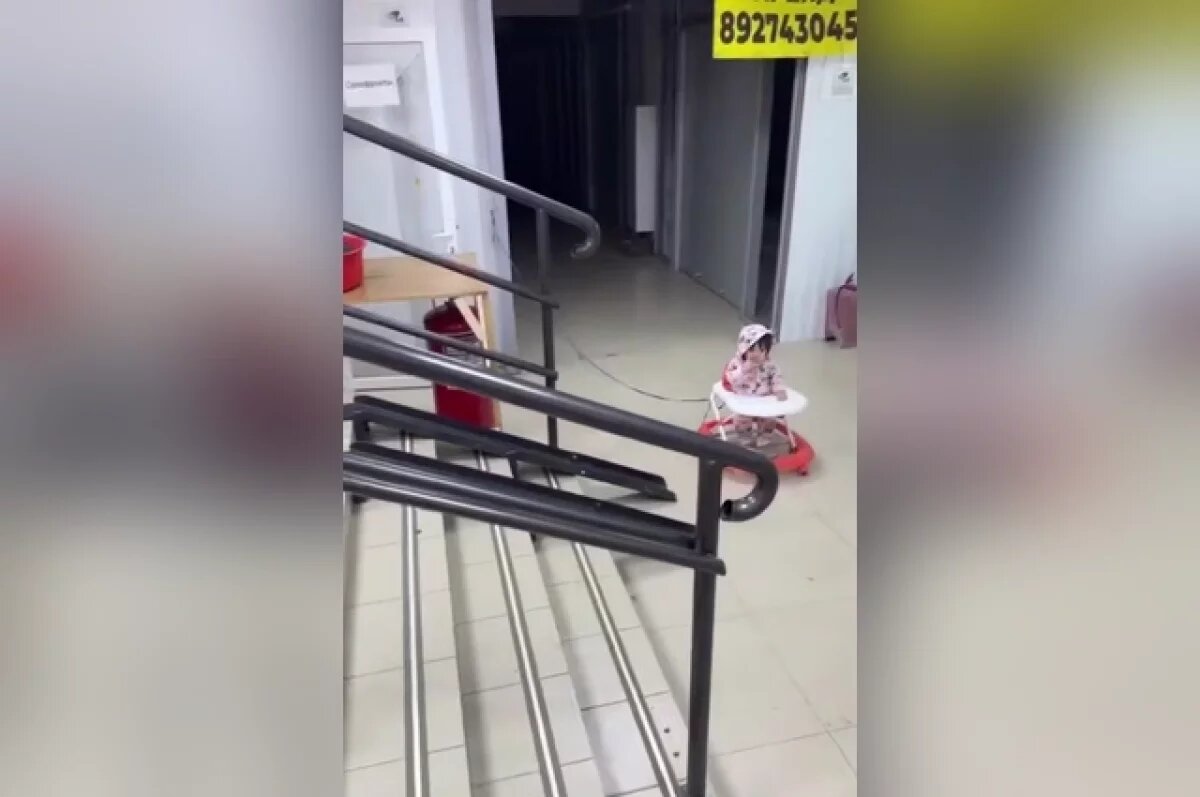    В соцсетях разлетелось шокирующее видео: в холодном коридоре казанского торгового центра к перилам привязана веревкой девочка в ходунках.