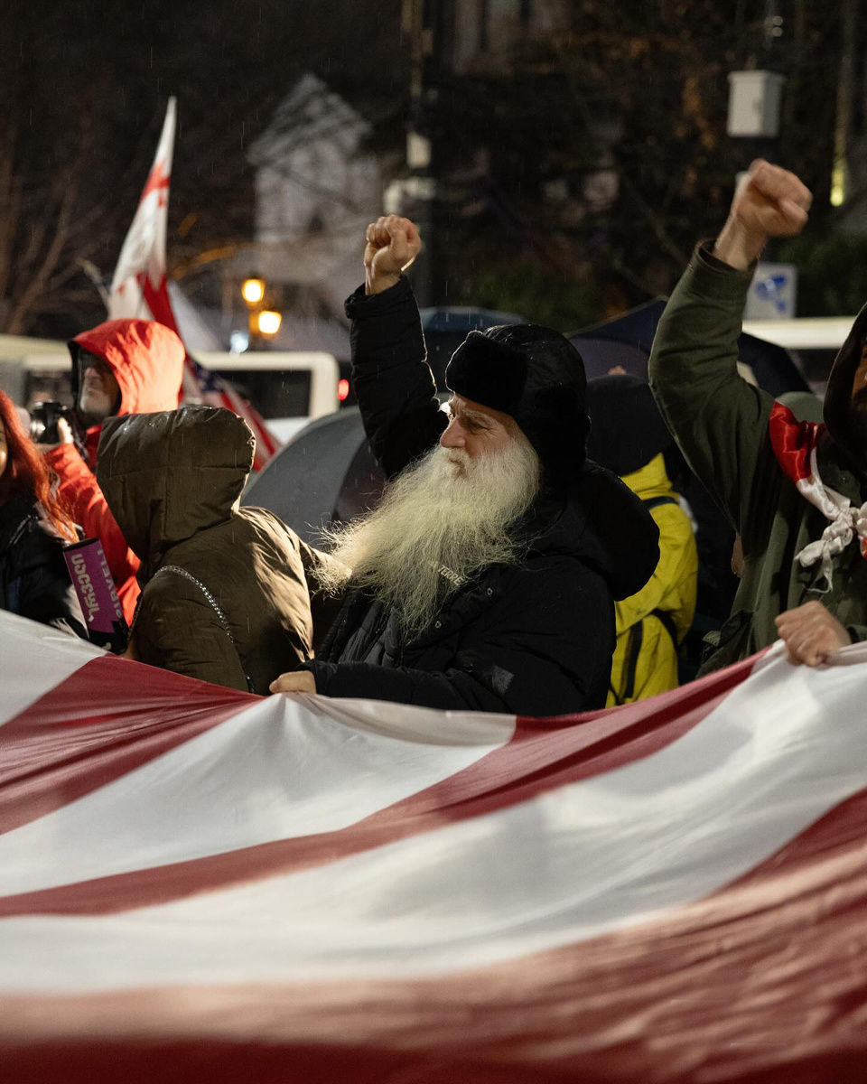 Архимандрит Дороте (Курашвили) вместе с оппозиционными активистами празднует удары США по Ирану в Тбилиси, держа американский флаг. 28 февраля 2026 г.