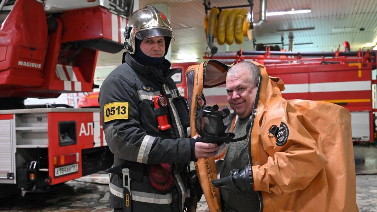    Старший инструктор газодымозащитной службы пожарно-спасательной части № 51 Руслан Марков помогает корреспонденту «Вечерней Москвы» Андрею Объедкову надеть спецкостюм для защиты от химических воздействий / Фото: Александр Кочубей / Вечерняя Москва