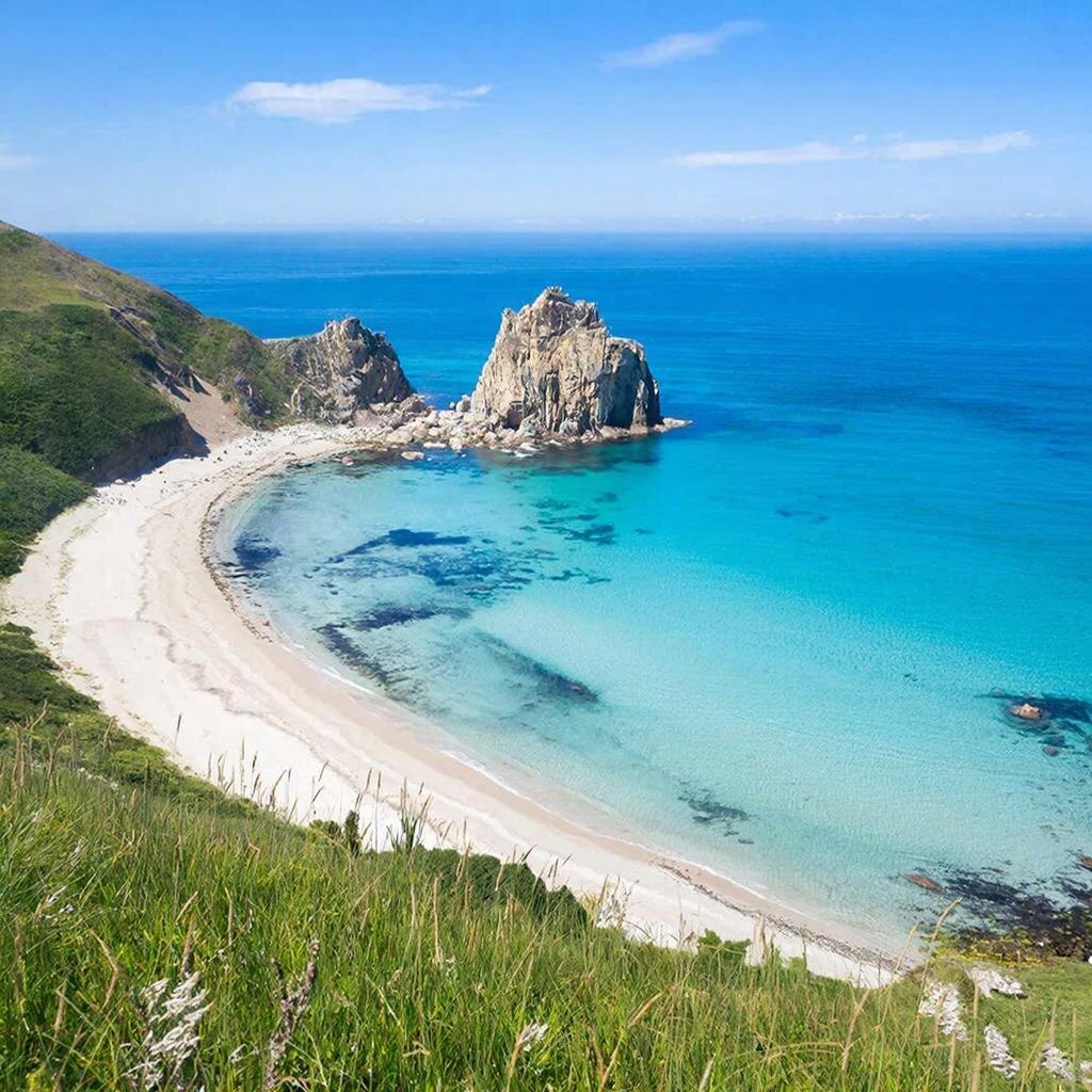 Бухта Триозёрье, Приморский край. Белый песок, бирюзовая вода Японского моря и скала Крейсер вдалеке. Это место называют «Приморскими Мальдивами». С 2026 года здесь меняются правила отдыха — машины больше не пустят на пляж. Подробности в статье