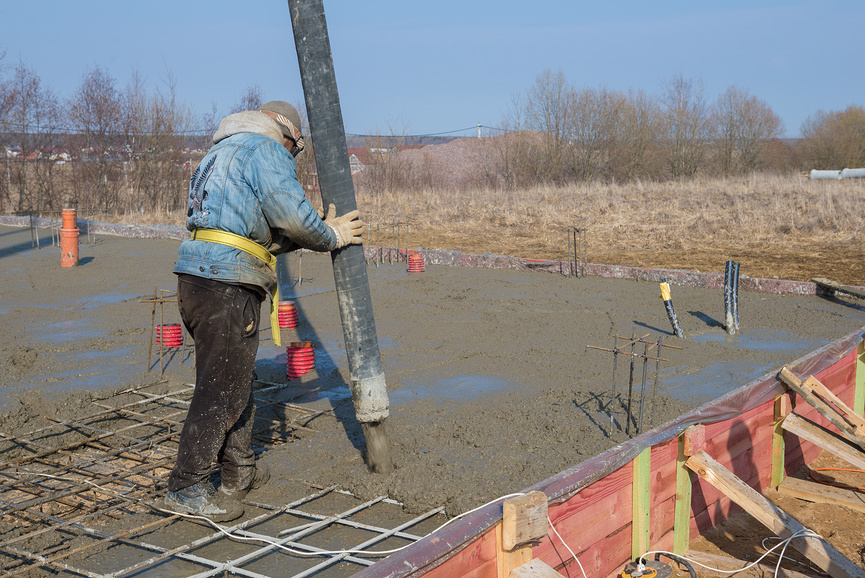 Строитель заливает бетонный фундамент для загородного строения