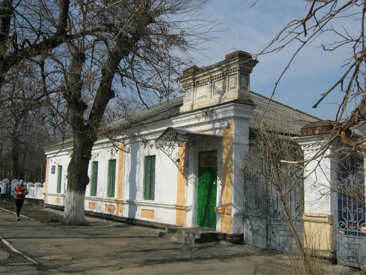 Офицерский клуб 8-го Астраханского Драгунского полка. Ссылка: https://vk.com/album-31220304_203076540 Здание построено в конце XIX в. Вход здания украшен богатым аттиком, украшенным филенками, выполненными из камня. Поле стены и оконные проемы оформлены скупо, тем не менее, здание изобилует  предметами декоративно-прикладного искусства – коваными воротами, калиткой и козырьком, демонстрирующие высокий уровень мастерства автора. Стилистическая схожесть со зданиями казарм позволяет говорить о том, что клуб был построен изначально Астраханским полком для своих нужд не позднее 90-х годов XIX в. Астраханский драгунский полк изначально был создан как кирасирский, прославился в Отечественной войне. В ознаменование заслуг кирасир в этой битве название Астраханского полка было запечатлено на стене храма Христа Спасителя, сооруженного в Москве в честь избавления от нашествия «двунадесяти языков». Это была высокая честь. Тем более, что ее удостоился совсем недавно созданный полк. Астраханский полк прибыл в 1890 году в Тирасполь и оставил немало наследия в архитектурном плане. Ссылка: https://tourismpmr.org/registry/oficzerskij-klub-8-go-astrahanskogo-dragunskogo-polka/  Для справки: 12.10.1811 — генерал-майором Бороздиным 2-м в м. Усвяты Велижского уезда Витебской губернии из офицеров и нижних чинов, отделённых от лейб-кирасирского Его Величества, лейб-кирасирского Её Величества, Екатеринославского кирасирского, Рижского, Казанского, Ямбургского, Нежинского, Псковского, Московского, Финляндского и Митавского драгунских, Гродненского, Елисаветградского и Изюмского гусарских полков сформирован Астраханский кирасирский полк в составе 5-ти эскадронов (ПСЗ, XXXI, 24808). Ссылка: https://ru.wikipedia.org/wiki/Астраханский_8-й_драгунский_полк 12 октября 2026 года исполняется 215 лет со дня сформирования Астраханского кирасирского полка. Астраханский кирасирский полк - 8-й драгунский Астраханский полк - 22-й драгунский Астраханский полк.