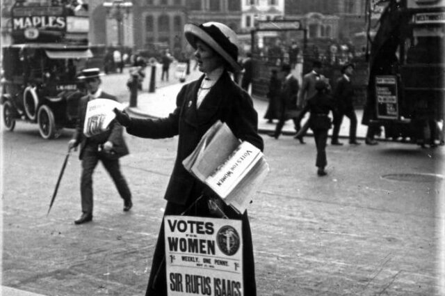 Британская суфражистка с плакатом раздает газеты или листовки на улице.  Снято до 1919 года