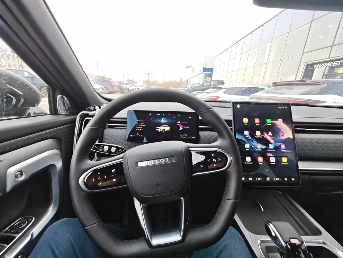Интерьер Jaecoo J7, место водителя. Широкоугольная камера телефона исказила картинку, из-за чего форма руля может показаться странной. На самом деле толщина баранки одинаковая. Есть только скос в нижней части.