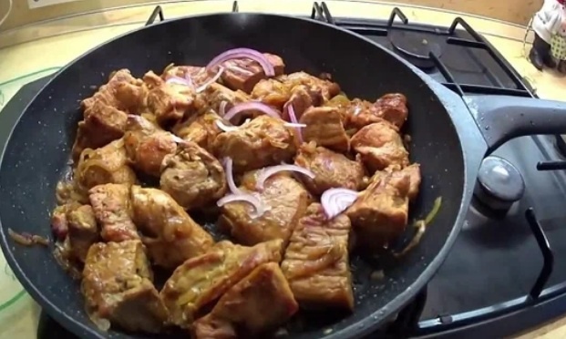 Свинина с луком и морковью на сковороде.