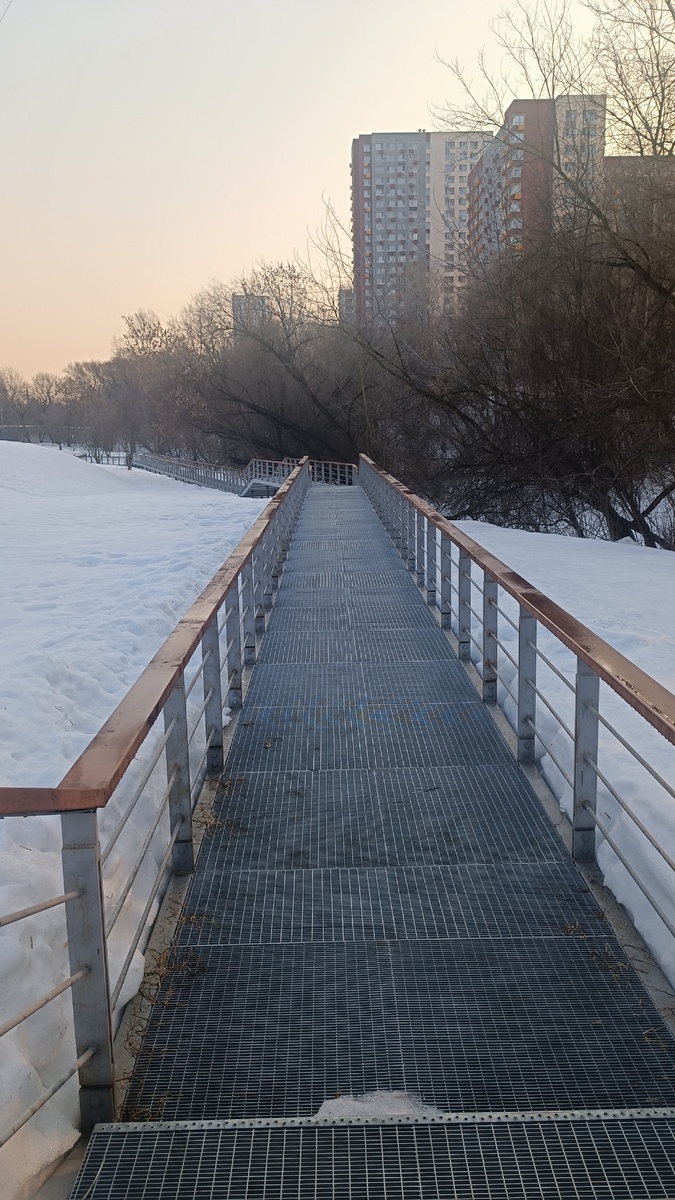 Слева метро, огороженное высоким забором, справа речка, вся в снегу.