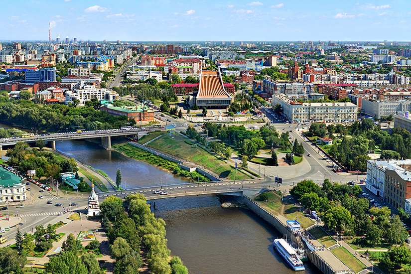 Панорама Омска с высоты: широкая река Иртыш, низкая застройка города и длинная линия горизонта.
