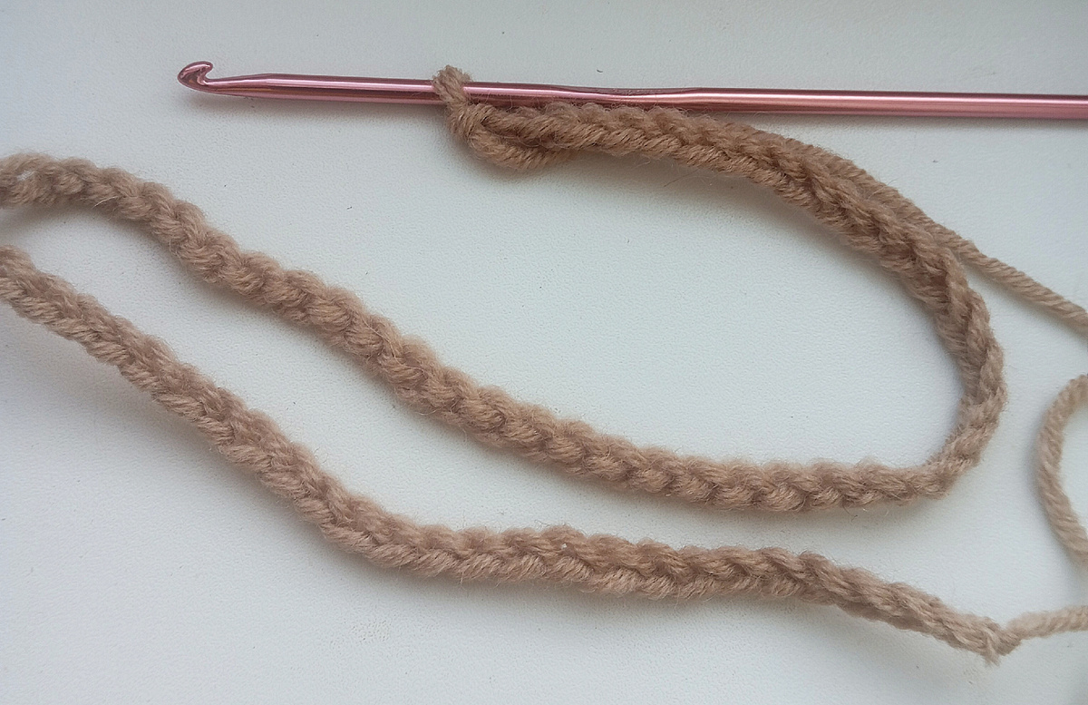 Цепочка воздушных петель связана. На переднем плане мы видим лицевую сторону. Она имеет вид косички. Выше лежит часть цепочки, повернутая к нам изнаночной стороной. На ней хорошо заметны протяжки между петлями. Именно их мы и будем использовать для набора петель.