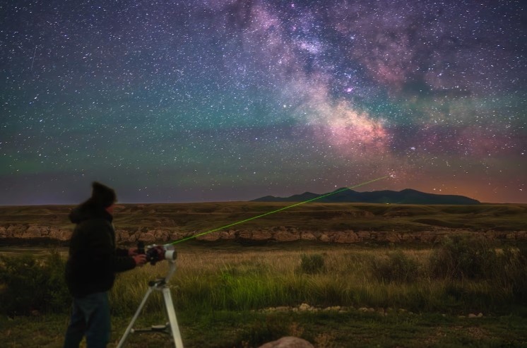 Фотограф Алан Дайер наблюдает за звездными скоплениями Мессье 7 и Мессье 6 у горизонта над холмами Свитграсс в Монтане — двумя объектами глубокого космоса, включенными в «Марафон Мессье».
