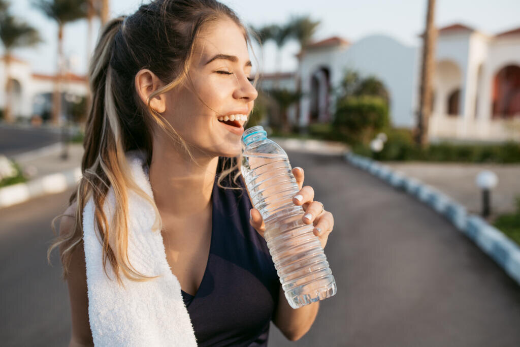    Closeup portrait excited happy young woman smiling with closed eyes to sun with bottle of water. Attractive sportswoman, enjoying summer, training, outwork, happiness Журналист