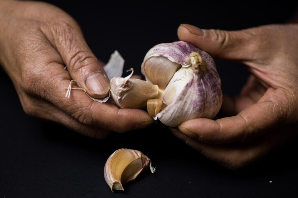    A closeup shot of a person peeling garlic in front of a black background Журналист