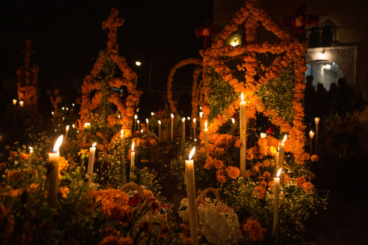 Могилы, украшенные бархатцами и свечами, на кладбище в ночь Дня мёртвых.