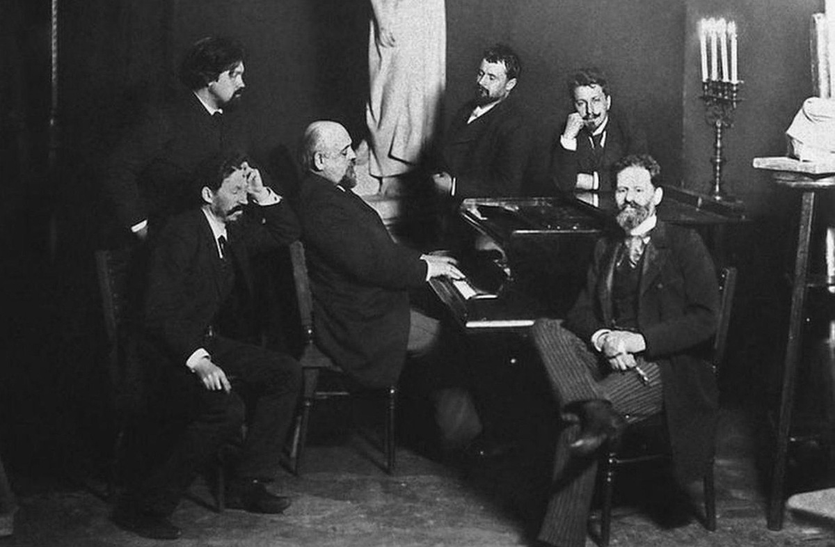 Участники Абрамцевского кружка в гостях у С.И. Мамонтова. Фотография. Слева направо: В.И. Суриков, И.Е. Репин, С.И. Мамонтов (за роялем), К.А. Коровин, В.А. Серов, М.М. Антокольский