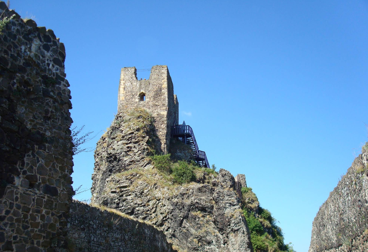 Внутренний вид руин замка Троски (Trosky Castle), каменная кладка средневековой башни, деревянная лестница для туристов, панорама Чешского Рая на фоне синего неба.