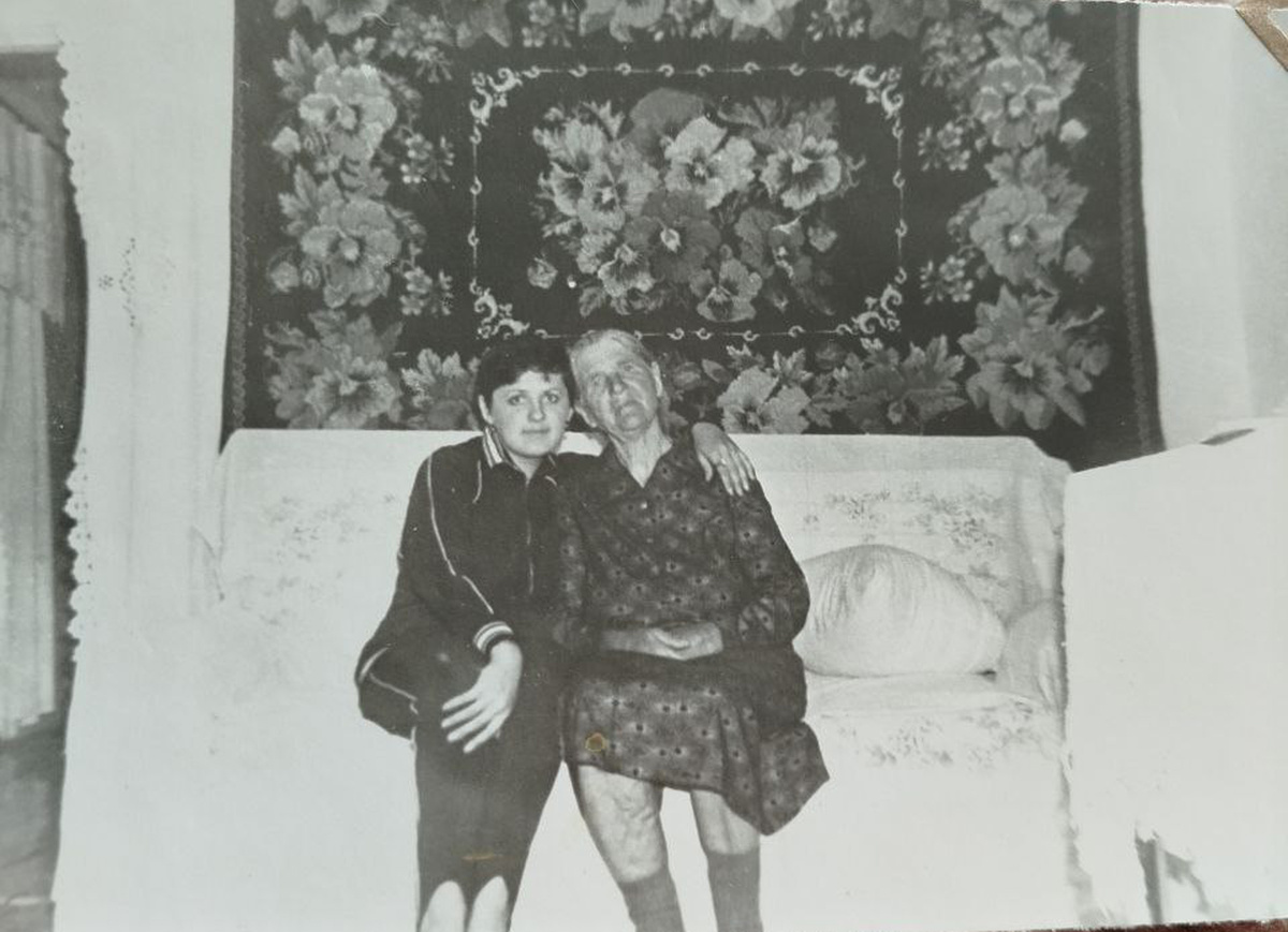 Светлана Комова с бабушкой на фоне ковра с фиалками