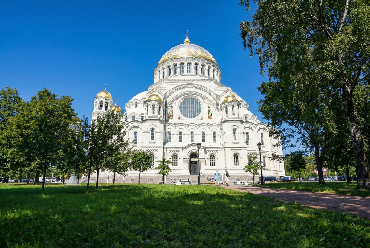 Величественный Морской собор святителя Николая Чудотворца в Кронштадте. Белоснежный храм в неовизантийском стиле с золотыми куполами эффектно возвышается на фоне ясного неба, окруженный сочной зеленью Якорной площади.