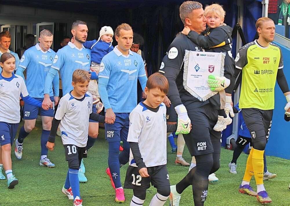 Дождались выхода стартовых составов команд и бригады судей в сопровождении детей. Обратите внимание, что капитан и вратарь "Крыльев" Сергей Песьяков (в черной футболке) и защитник Никита Чернов (третий слева в голубой майке) с двумя ребенками вышли на поле.