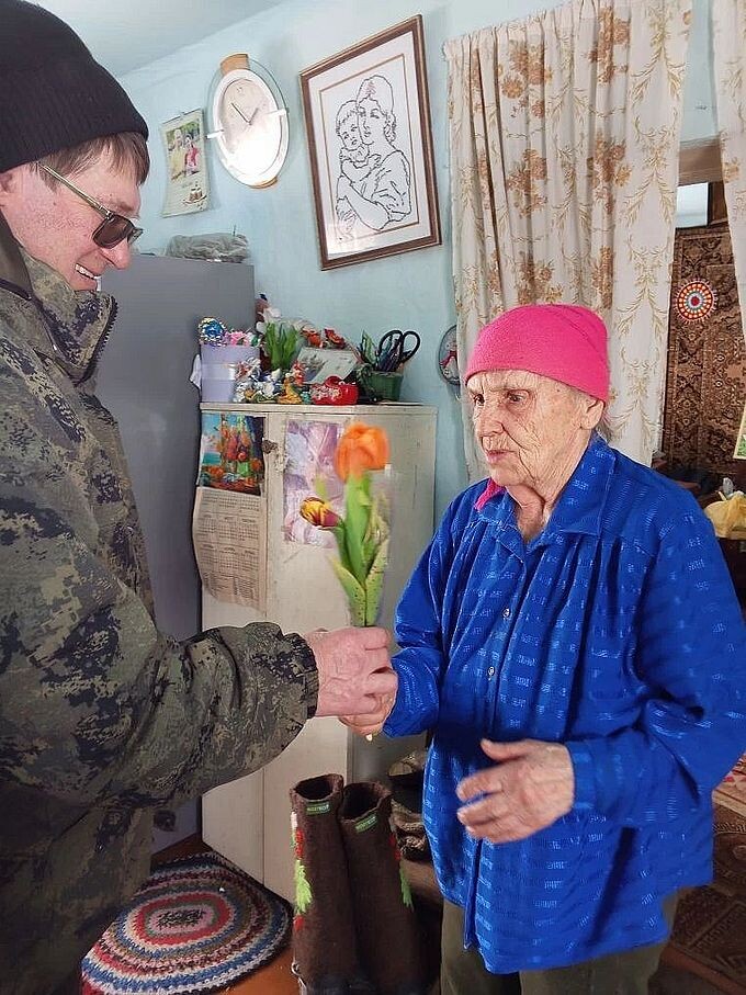 Социальный работник дарит пожилой женщине тюльпаны