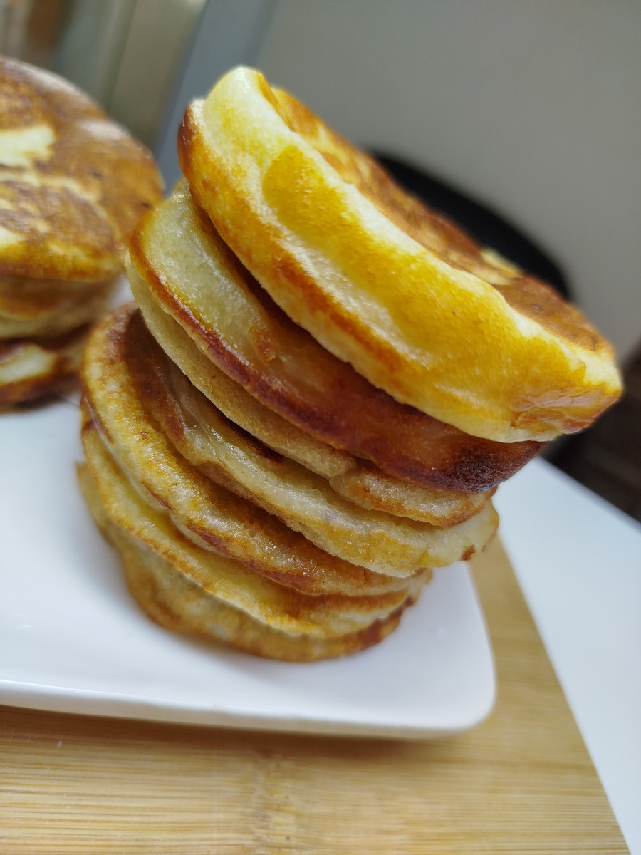 В большую миску отправляем тёплое молоко 350 гр, дрожжи, сахар, тщательно перемешиваем и добавляем всю муку и манку. Перемешали и оставили на 30-60 минут под крышкой ( до первого подъёма).
 После первого подъёма перемешать тесто и поставить до второго подъёма примерно на 40 минут.
В другой миске разбиваем яйца,  размешать венчиком. Подогреть 150 гр молока.
Когда тесто поднялось второй раз, добавляем:  яйца, соль, перемешиваем. Вливаем горячее молоко и растительное масло. Все перемешать. Тесто готово.
Разделить тесто на две миски . В одну добавить нарезанное почищенное от кожуры яблоко, в другое нарезанный банан. Нарезать кубик примерно 5 мм.

Жарим около минуты с первой стороны, со второй 30 секунд.