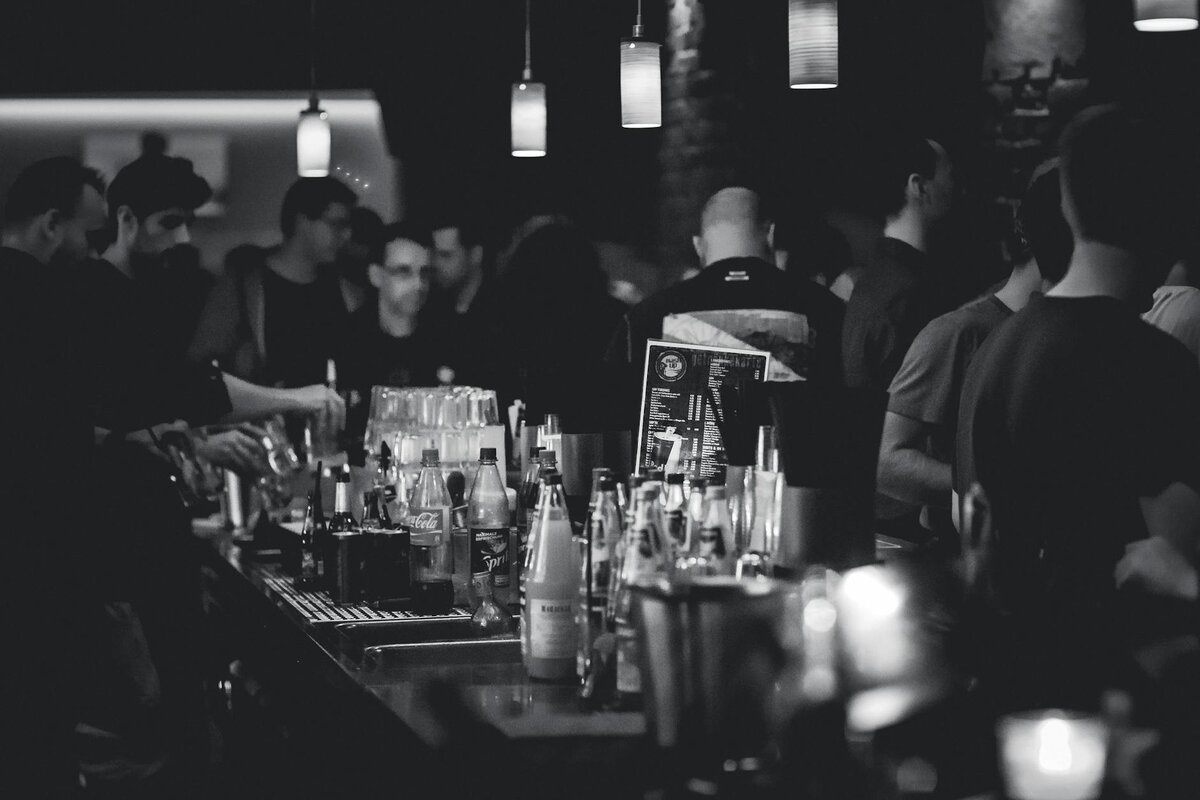 Black and white photo capturing the lively atmosphere in a bar with people socializing and a busy ba