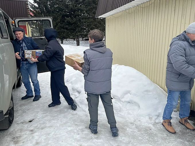 Дети вместе со взрослыми передают посылки для погрузки в автомобиль