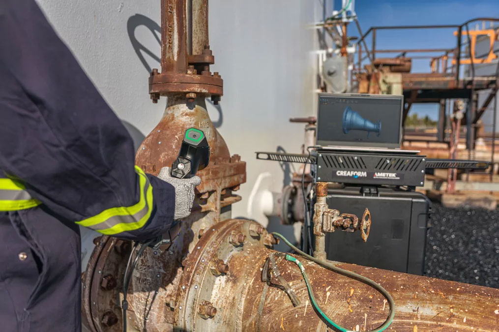 Специалист по неразрушающему контролю держит 3D-сканер метрологического класса и проводит осмотр коррозии на корродированном клапане.