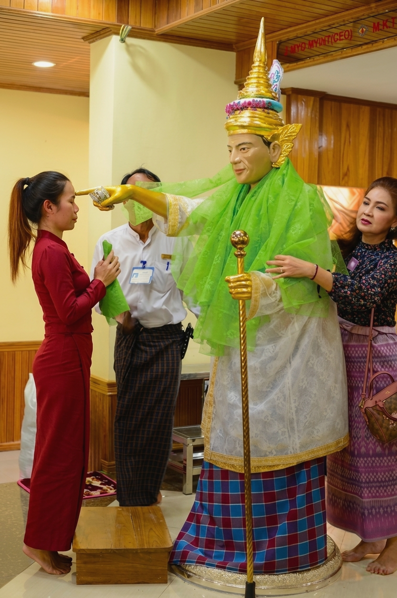 Тайская туристка загадывает желание, прикоснувшись лбом к статуе Бо Бо Джи в пагоде Ботатаунг, в то время как другая посетительница оборачивает статую тканью в знак почтения. Фотография из книги «BOBOGYI: A Burmese Spiritual Figure».