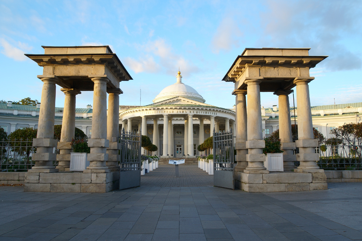 Пропилеи — ворота в мир милосердия: На переднем плане расположены монументальные парные павильоны-пропилеи. Их массивные колонны и строгие формы создают чёткую визуальную границу, отделяющую суету города от умиротворённого пространства «дворца милосердия». Раскрытые кованые ворота приглашают зрителя зайти внутрь.