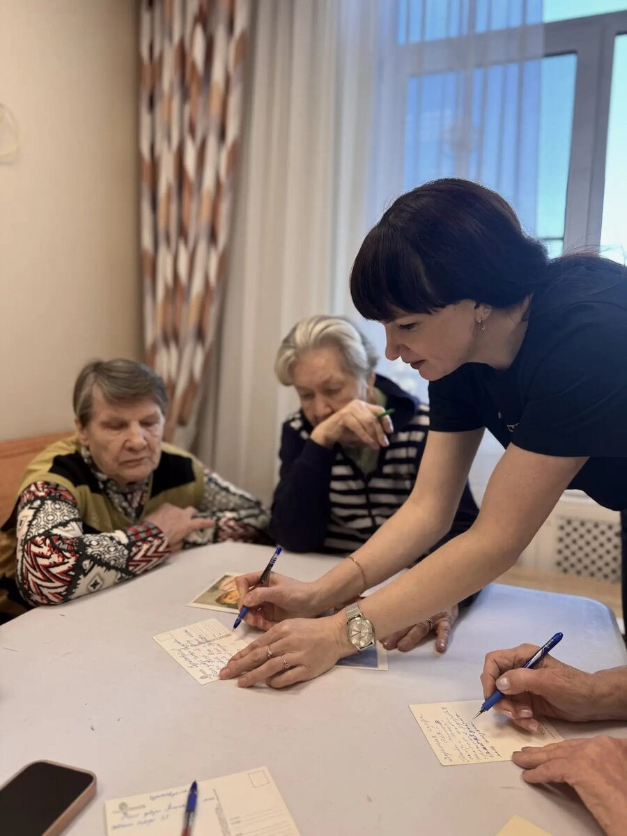 Людмила Анатольевна показывает Тамаре Федоровне, как рисовать смайлики на обороте открытки. 