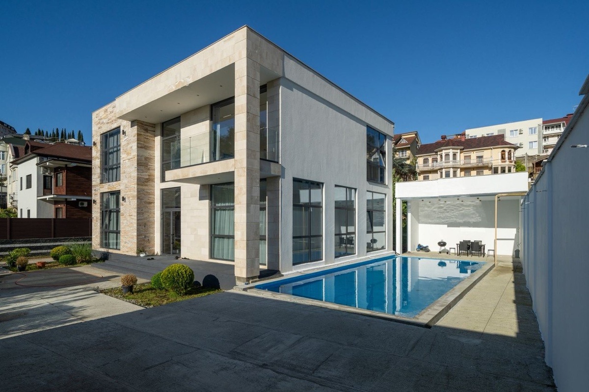 Внешне вилла решена в современной эстетике с прямой геометрией, светлыми фасадами и крупными стеклянными плоскостями