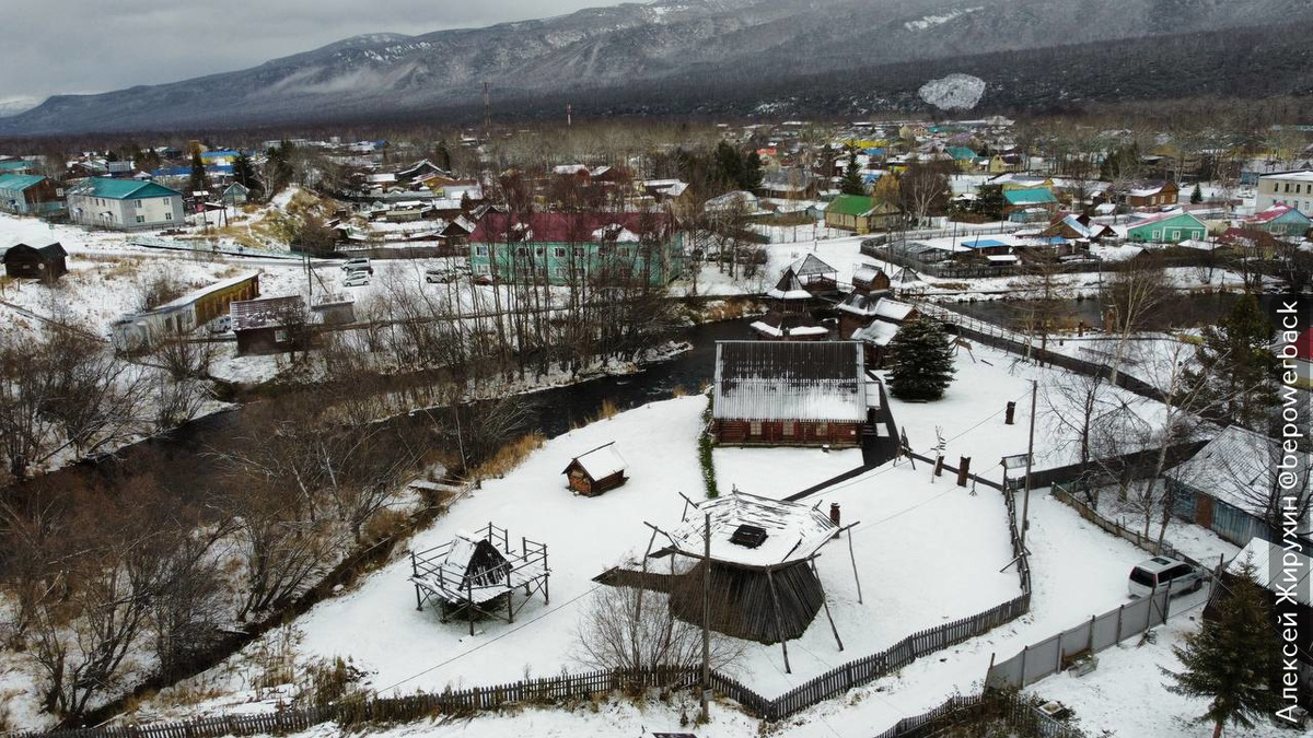 Село Эссо на Камчатке. На переднем плане - реплики традиционных ительменских жилищ. Выглядят как приземистые деревянные конструкции среди снега.