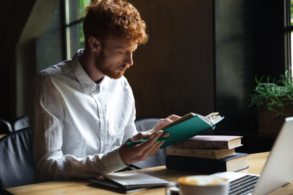    Photo of concentrated readhead bearded student, preparing for university exam in a cafe Журналист