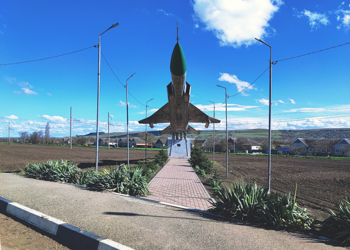 Дорога, распаханное поле, за которым виднеются сельскиие домики... и истребитель-перехватчик. Вот так соседство.