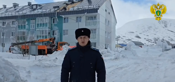 Прокурор Северо-Курильского района Виталий Кочев на фоне одного из многоквартирных домов с повреждённой кровлей / фото: канал прокуратуры Сахалинской области в Мах