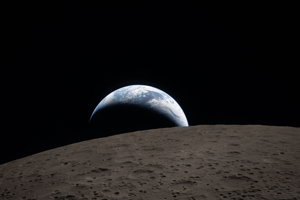 Закат Земли, снятый через иллюминатор Orion 6 апреля во время облёта Луны. За испещрённой кратерами лунной поверхностью виднеется приглушённо-голубая Земля с ярко-белыми облаками. На тёмной стороне Земли наступает ночь. На освещённой стороне над Австралией и Океанией видны клубящиеся облака. Кратер Ом на переднем плане имеет террасированные края и плоское дно, прерываемое центральными пиками. Фото: NASA 