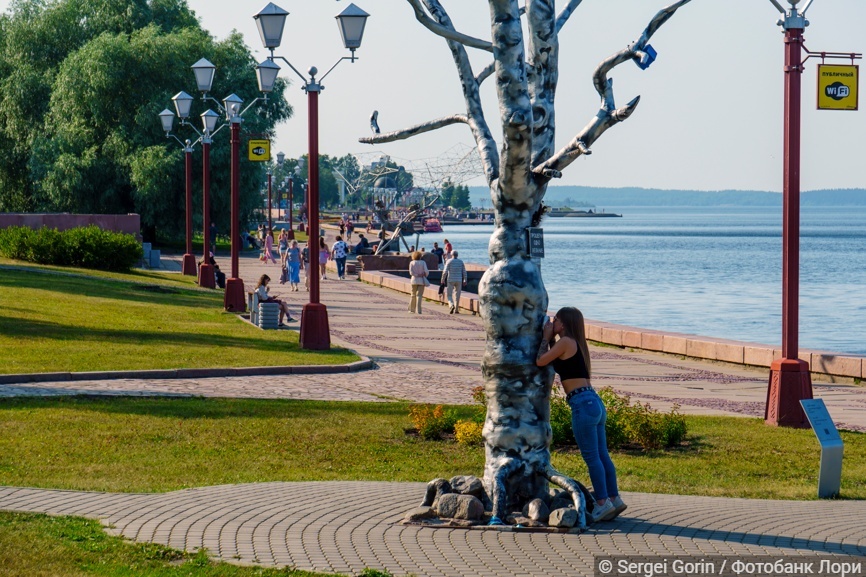 Девушка шепчет желание в ухо дереву желаний на набережной Онежского озера в городе Петрозаводске
