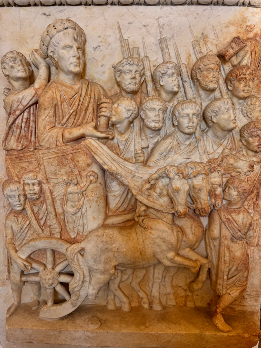 триумфатор на колеснице, запряжённой лошадьми, вокруг легионеры с копьями, дети у колеса. Музей в Палестрине, Италия