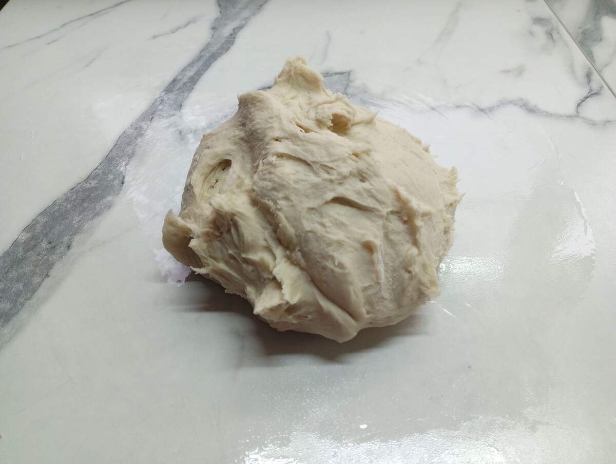 Вымешанное тесто на рабочей поверхности, смазанной тонким слоем масла