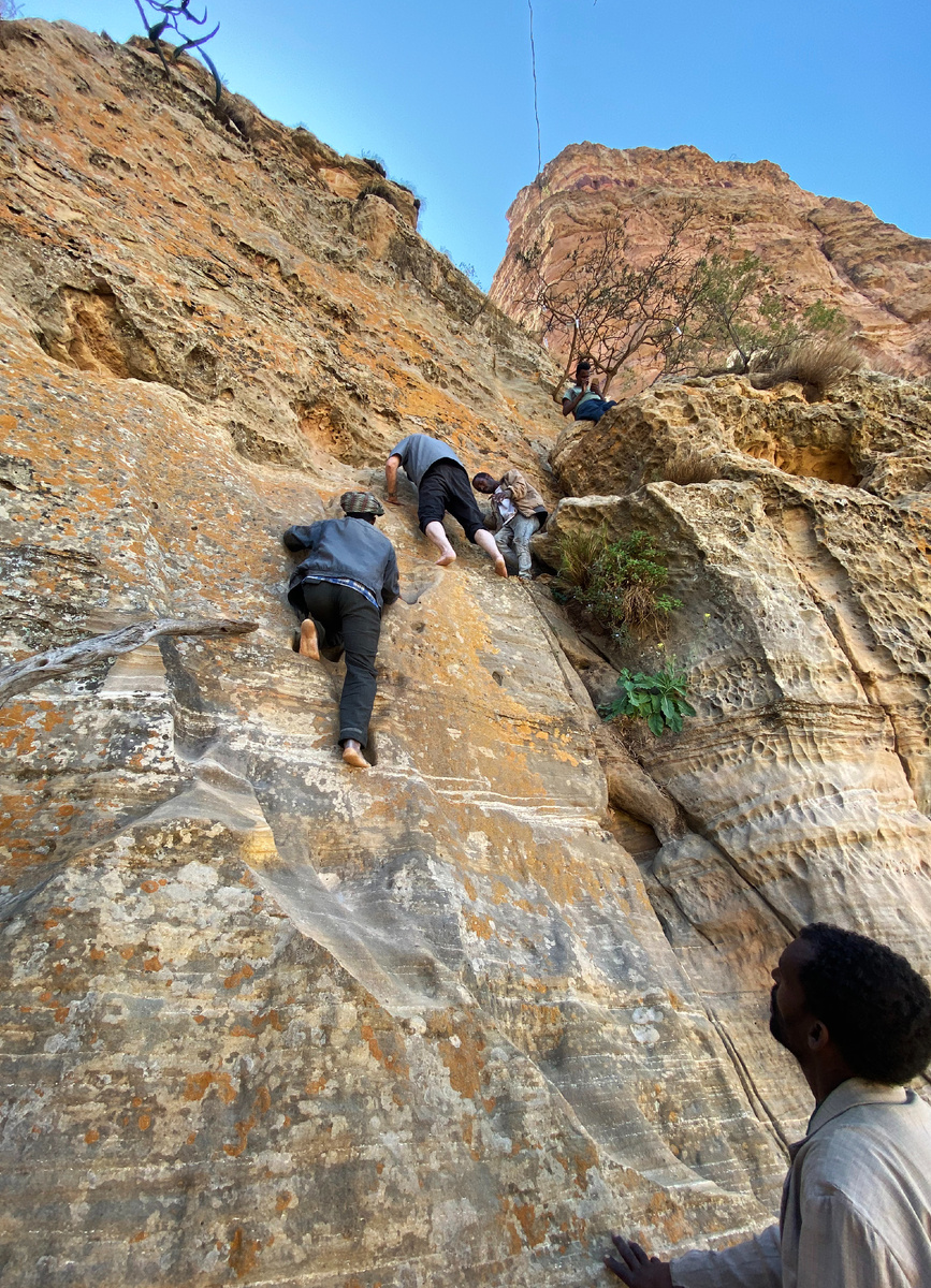 Паломники лезут на отвесную скалу босиком.  Изображение взято с сайта https://upload.wikimedia.org/wikipedia/commons/e/eb/Abuna_Yemata_Guh_entryway_climb.jpg