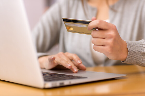 Close-up woman's hands holding a credit card and using computer keyboard for online shopping / Shutterstock   📷