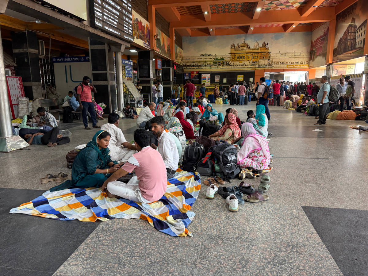 Зал ожидания вокзала. Семьи сидят на полу на покрывалах, ждут поезд.